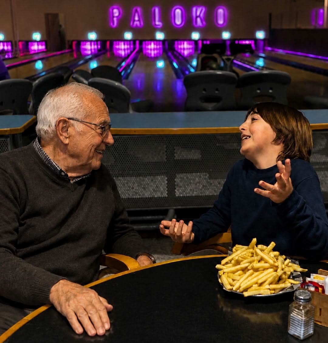 Abuelo y nieto compartiendo papas fritas frente a las pistas neón de Paloko