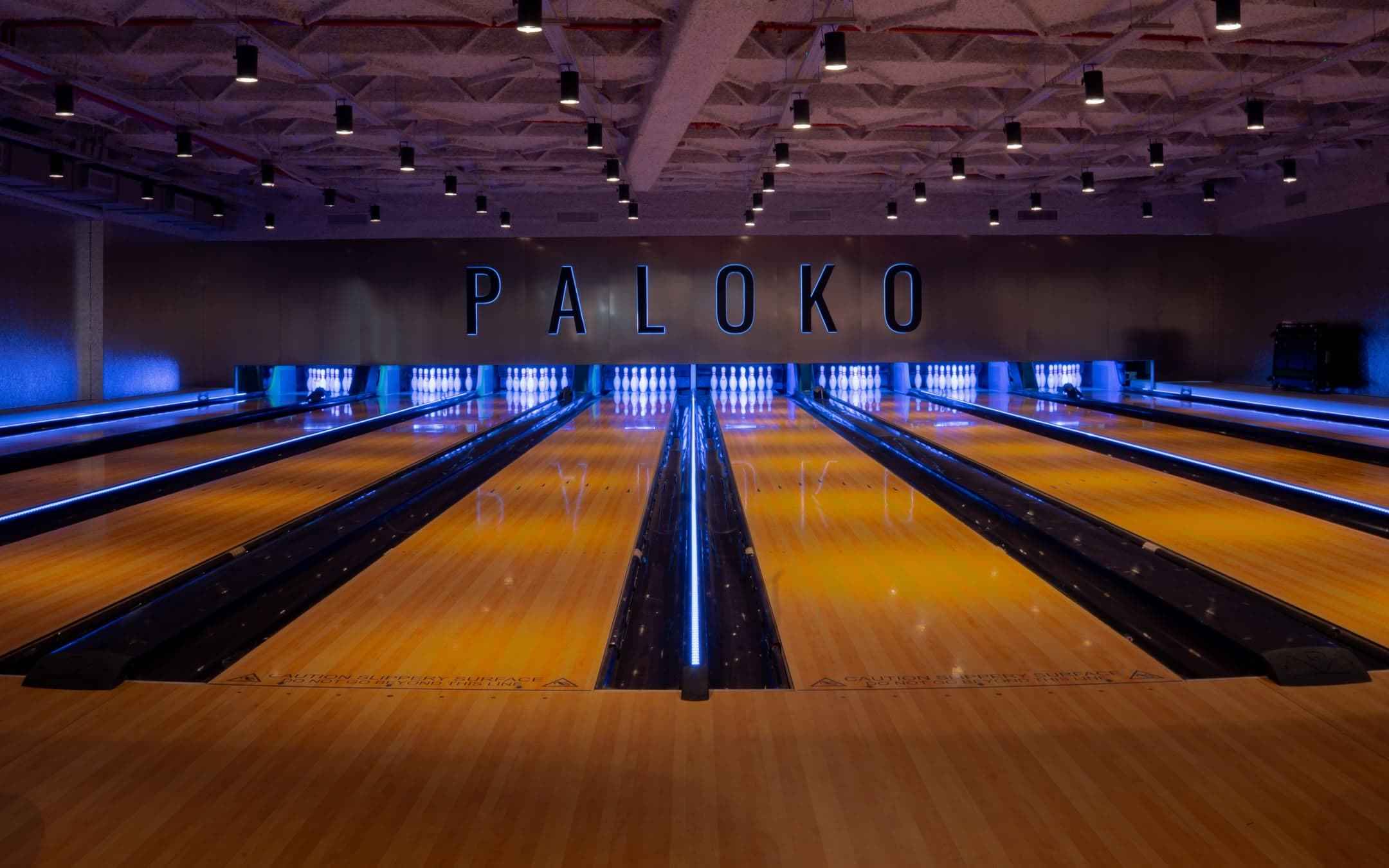 Pistas de Paloko: madera brillante, neón azul y el cartel PALOKO al fondo